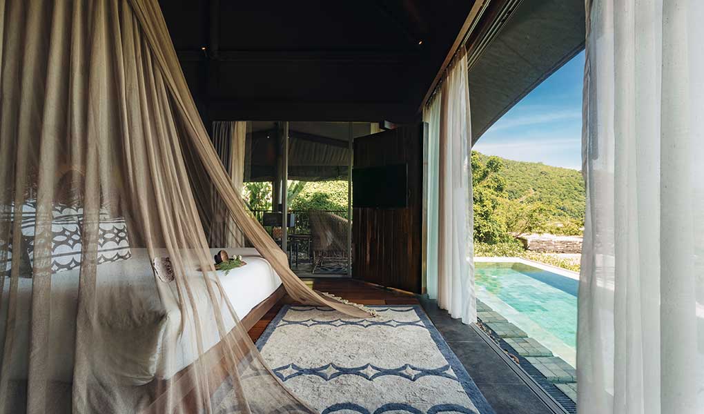 Interior de la villa con detalles de la cama y vistas a la piscina